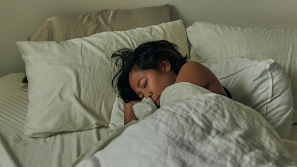 A person sleeps peacefully under white bedding in a softly lit bedroom.