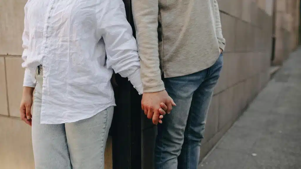 A couple standing back-to-back while holding hands on a sidewalk.
