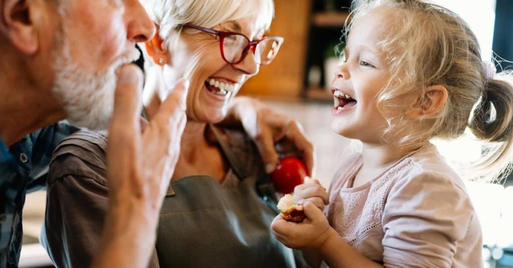 A joyful toddler laughing with smiling grandparents while holding a snack.
