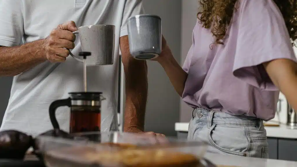 A man and woman holding mugs while standing in the kitchen.
