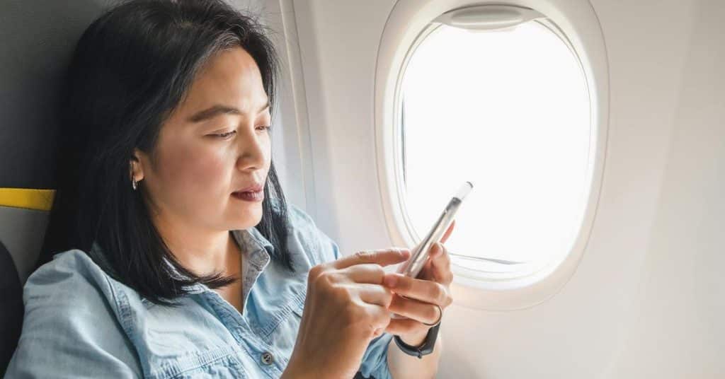 A woman using her smartphone while seated by an airplane window.