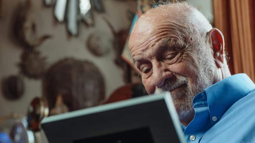 An older man with a white beard looks down at a framed object in hands.