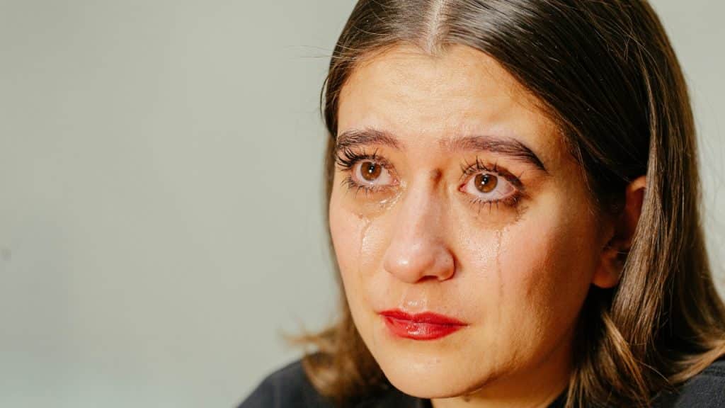 Close-up of a person with dark hair crying, with visible tears on their cheeks.