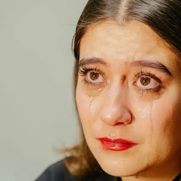 Close-up of a person with dark hair crying, with visible tears on their cheeks.