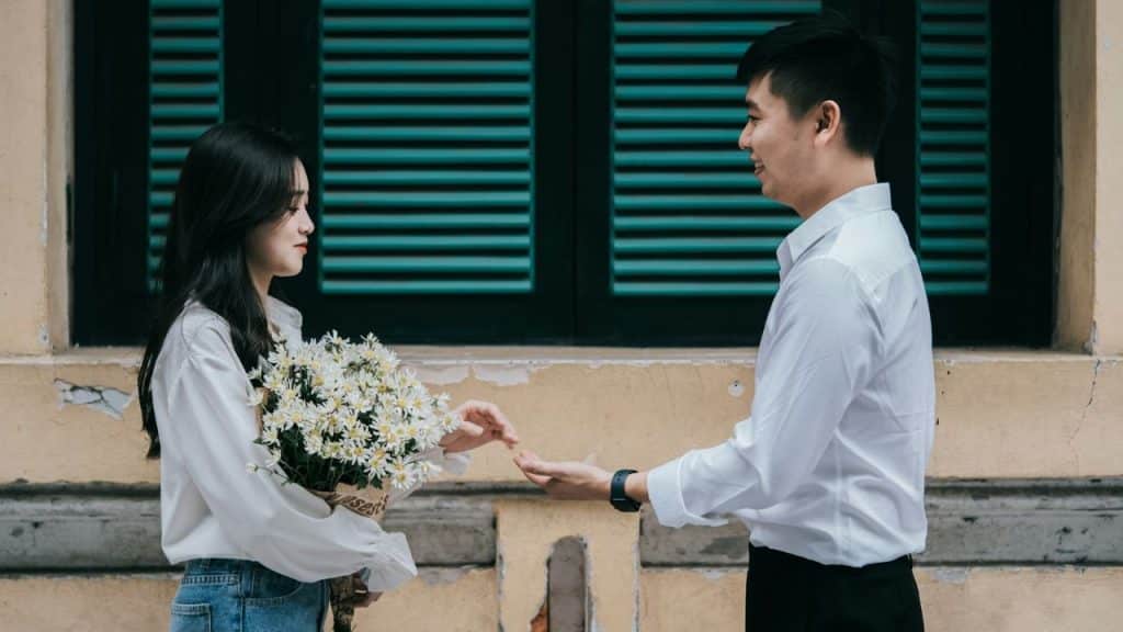 A man reaches out his hand toward a woman who is holding a white bouquet.