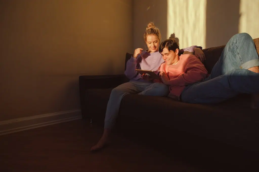 Couple Sitting on Brown Sofa while Using Digital Tablet