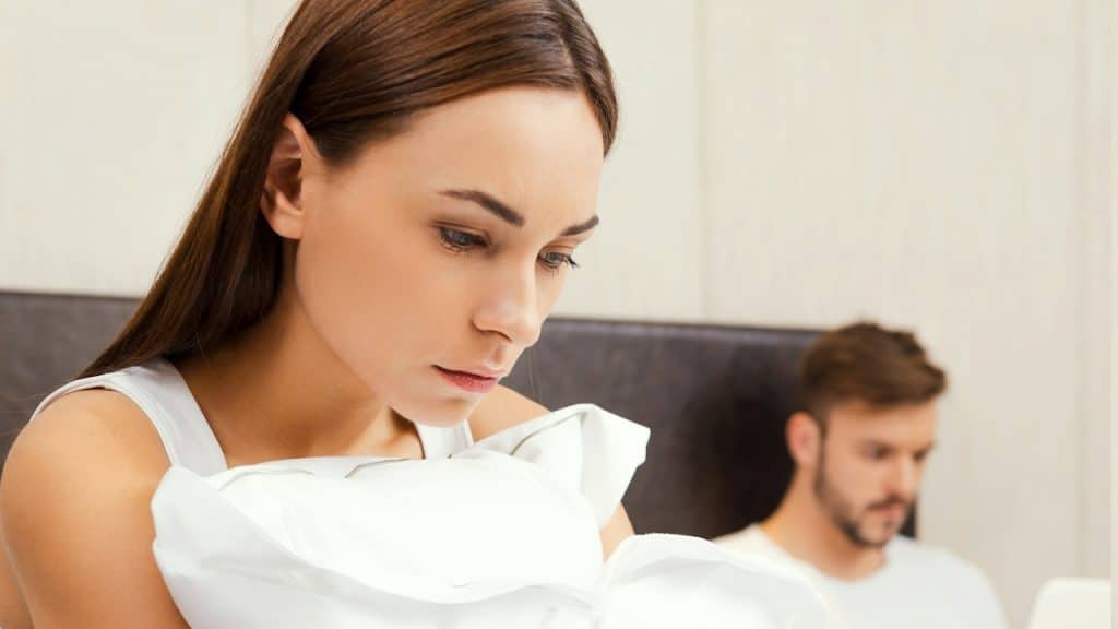 A sad couple sitting on a bed after an argument.