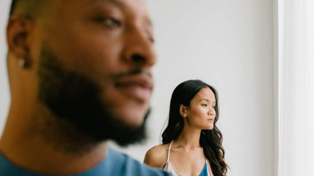 A couple standing seprately are looking at one side of the room.