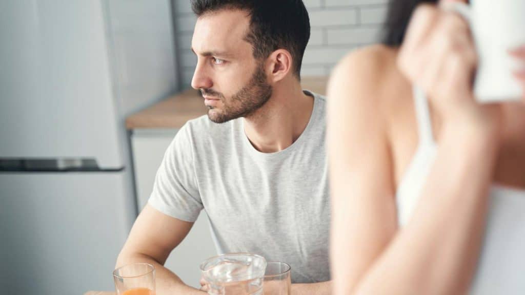 A thoughtful man is sitting in the kitchen and is looking away.