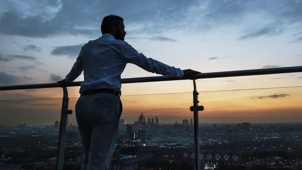 A man leaning against a rail by the sea at sunset and looking to the side.