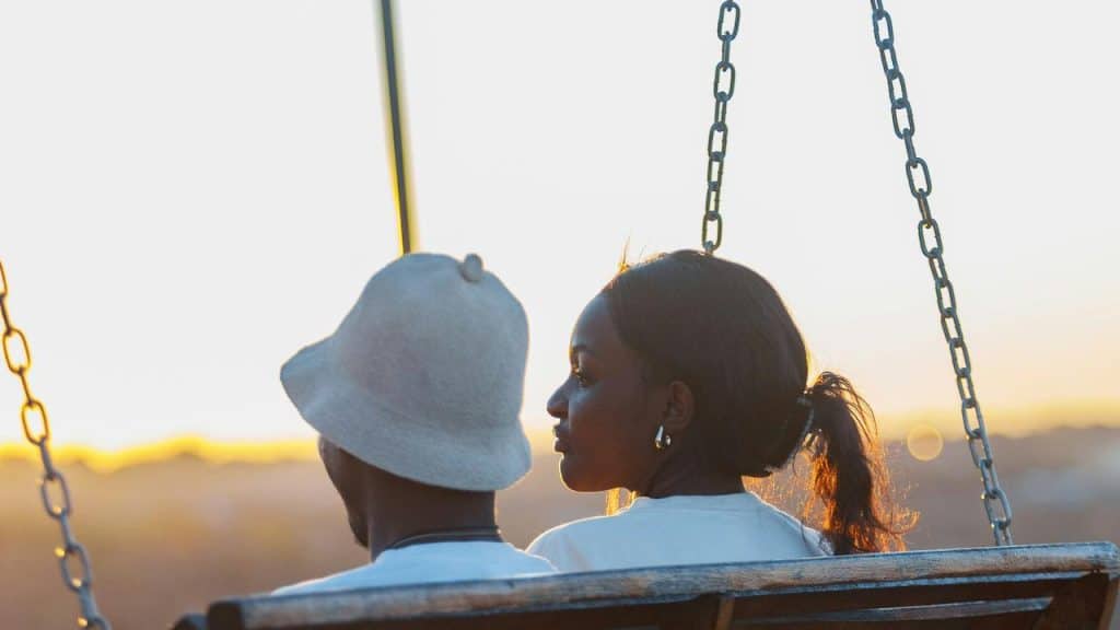 A couple sits on a swing together while watching the sunset.