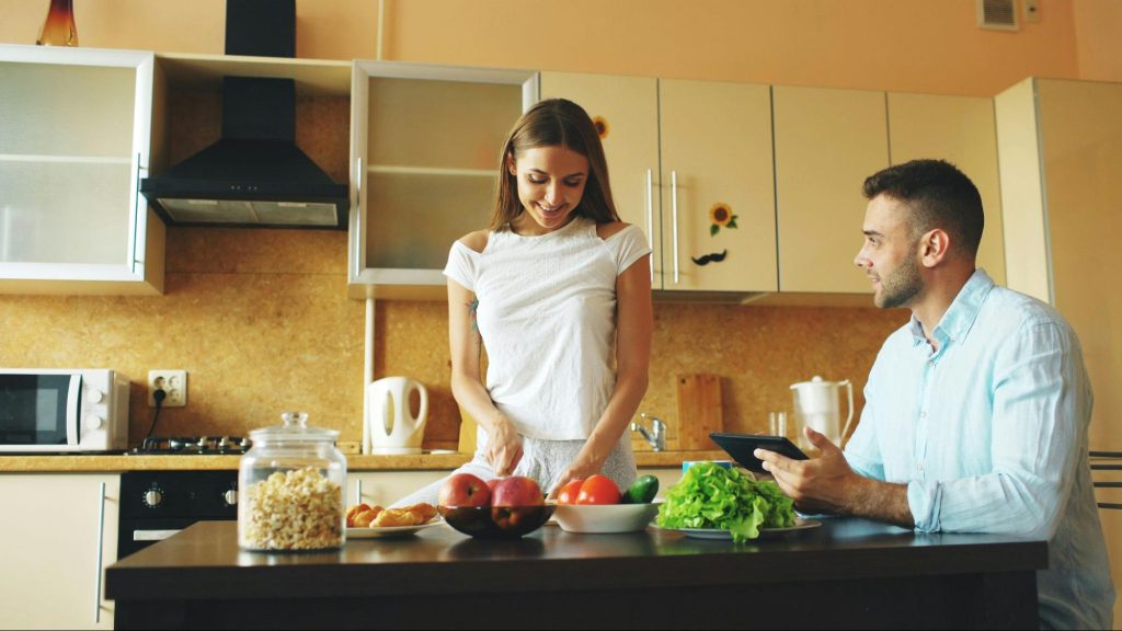 A woman cooking and a man waiting for her