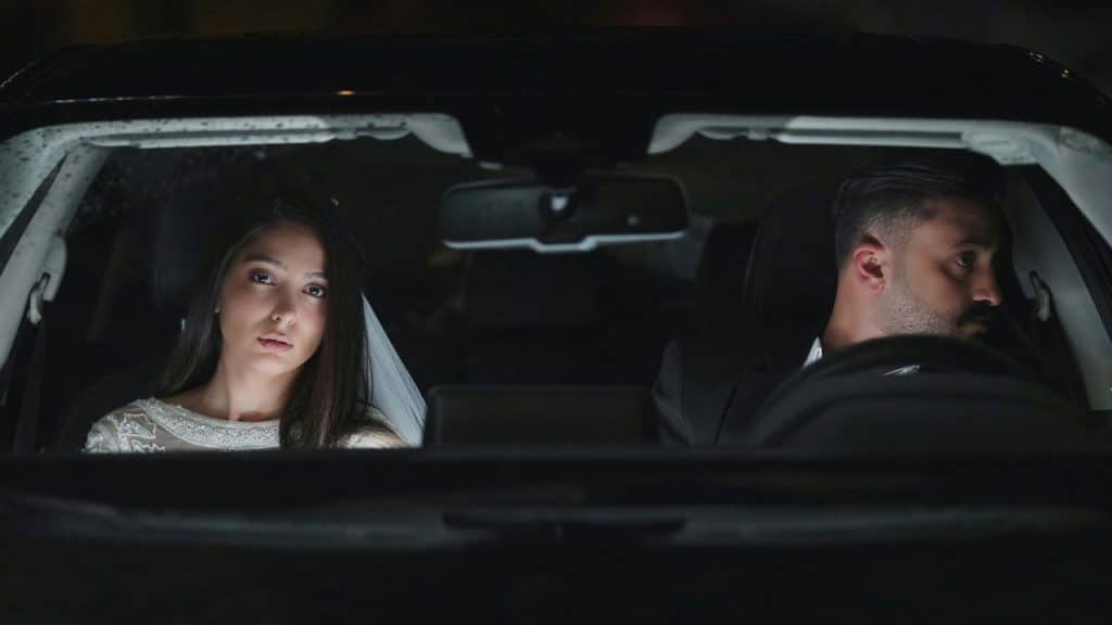 A woman in a white dress and a man in a suit sit in a car.