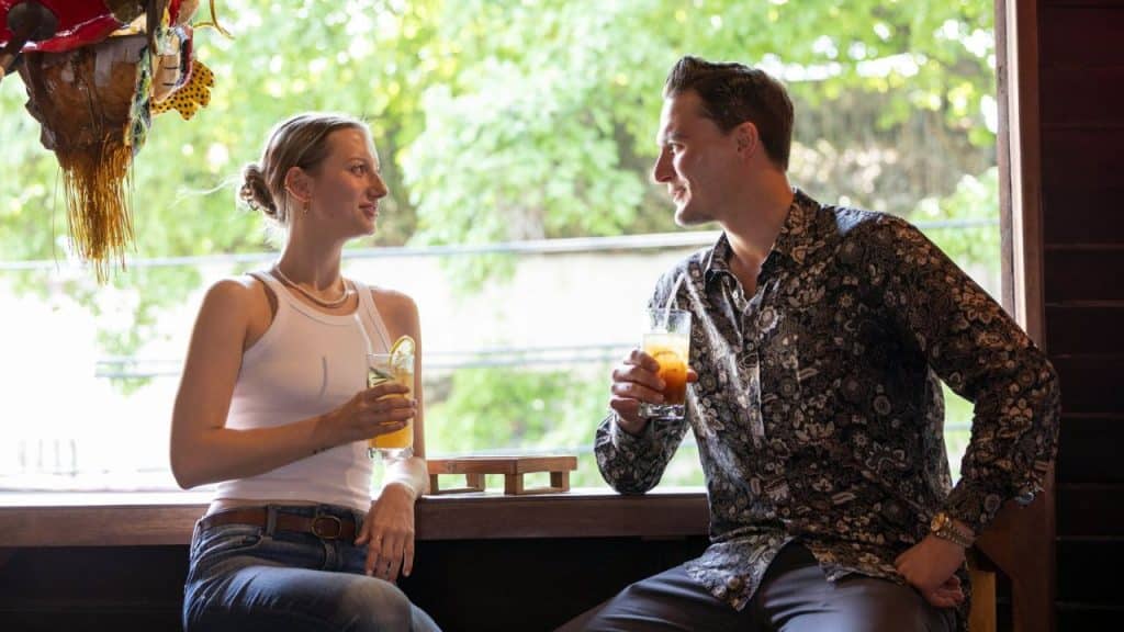 A man and woman sit at a bar holding drinks and looking at each other.