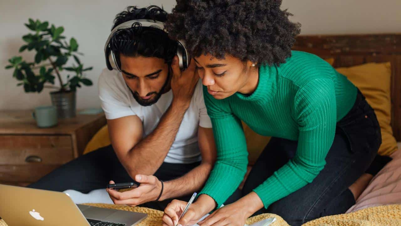 A couple working together at home, using a laptop and taking notes.