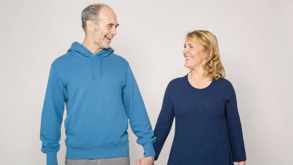 A man in a blue hoodie and a woman in a dark shirt hold hands.
