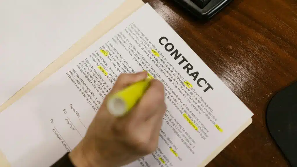 A hand uses a yellow highlighter to mark specific lines on a printed contract document.