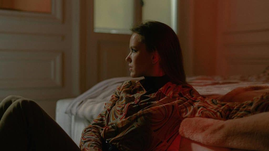 A woman sitting on a bed and looking thoughtfully into the distance.
