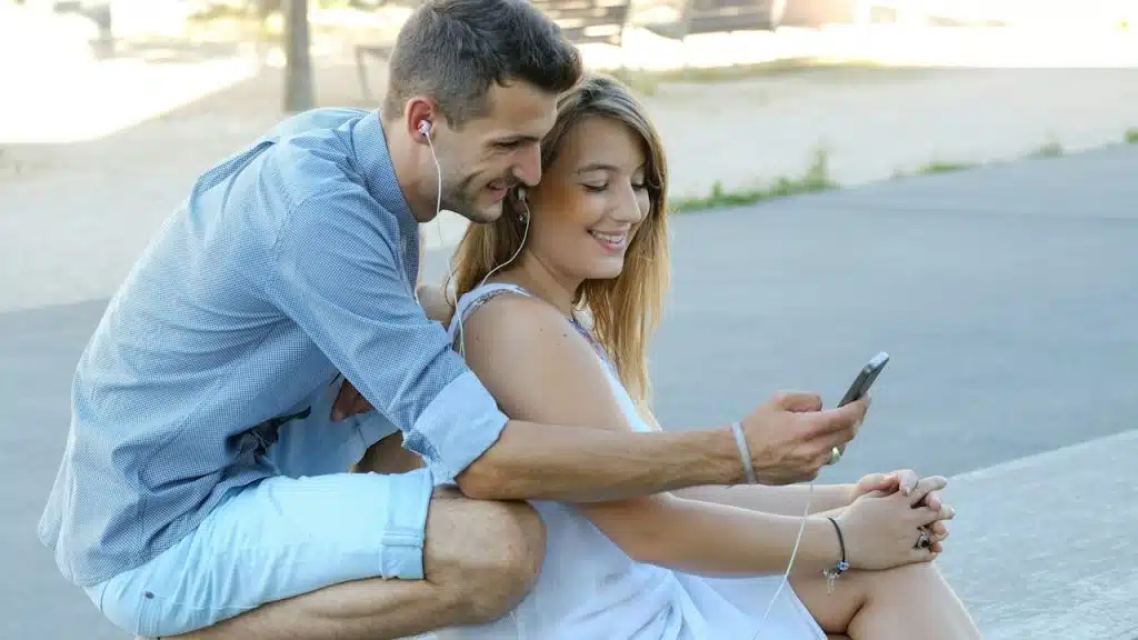 A couple with hands-free on sitting outdoors looking at a cellphone.