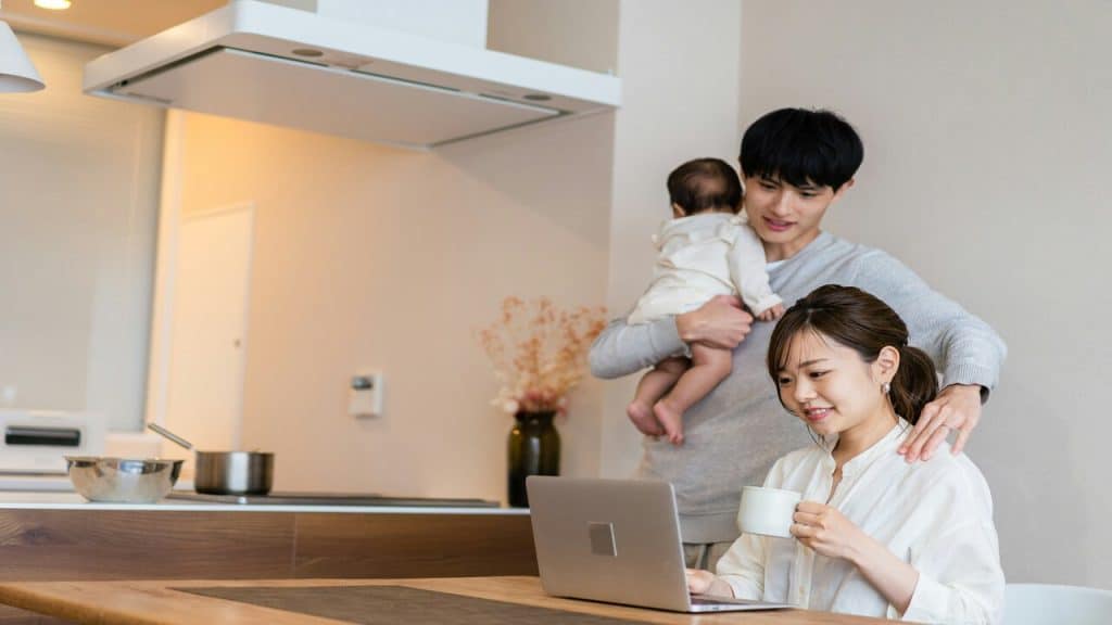 A man carrying their baby while his wife works
