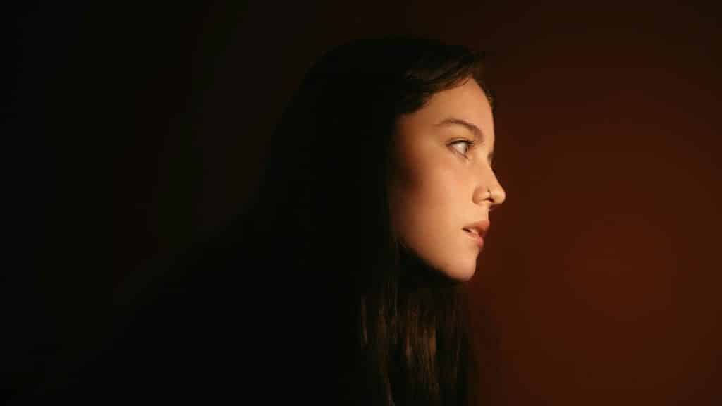A woman in profile lit softly against a dark background.