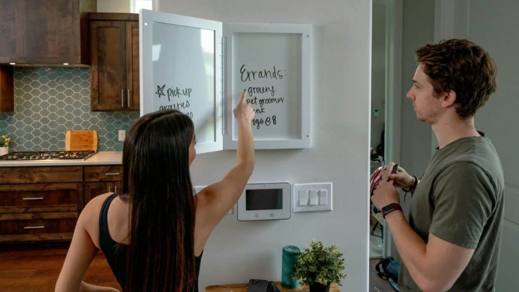 A woman points at a white errand board while a man stands nearby holding a pen.