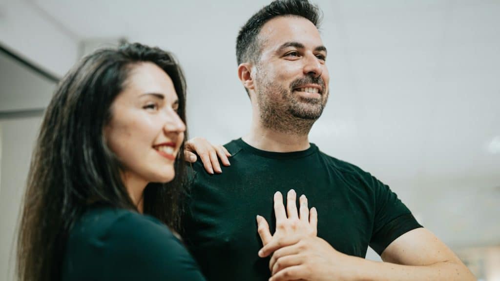 A woman resting her hand on a bearded man’s chest as they both smile.