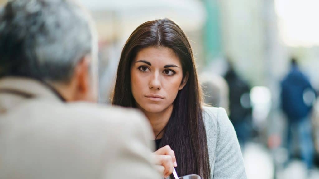Close-up of a woman with long dark hair looking toward a person whose back is turned.