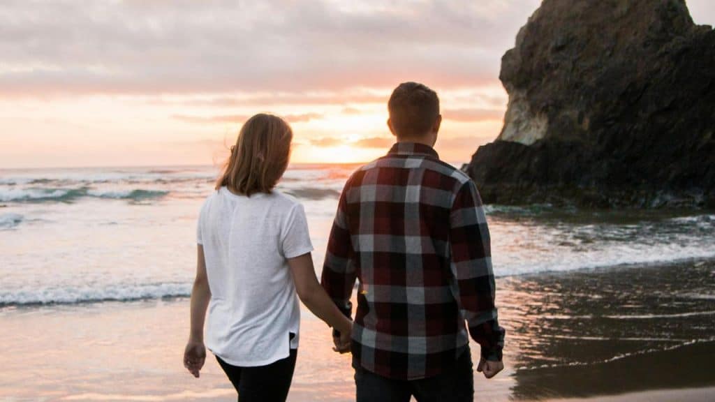 A couple holding hands while standing on the beach at sunset.