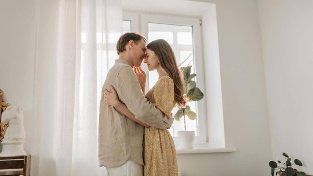 A couple embracing tenderly in a sunlit room by a window.