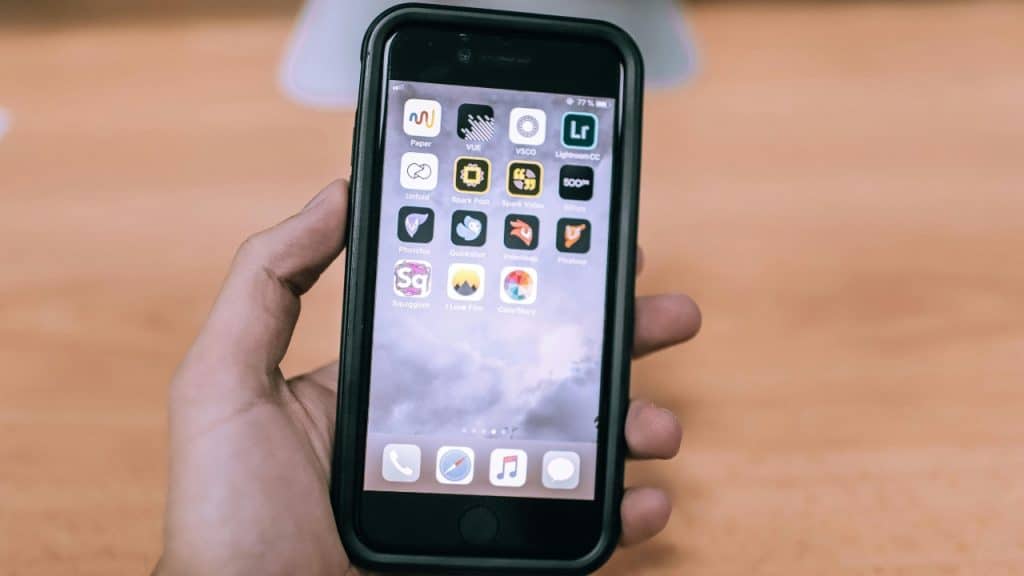 A hand holds a smartphone displaying various colorful app icons on the home screen over wood.