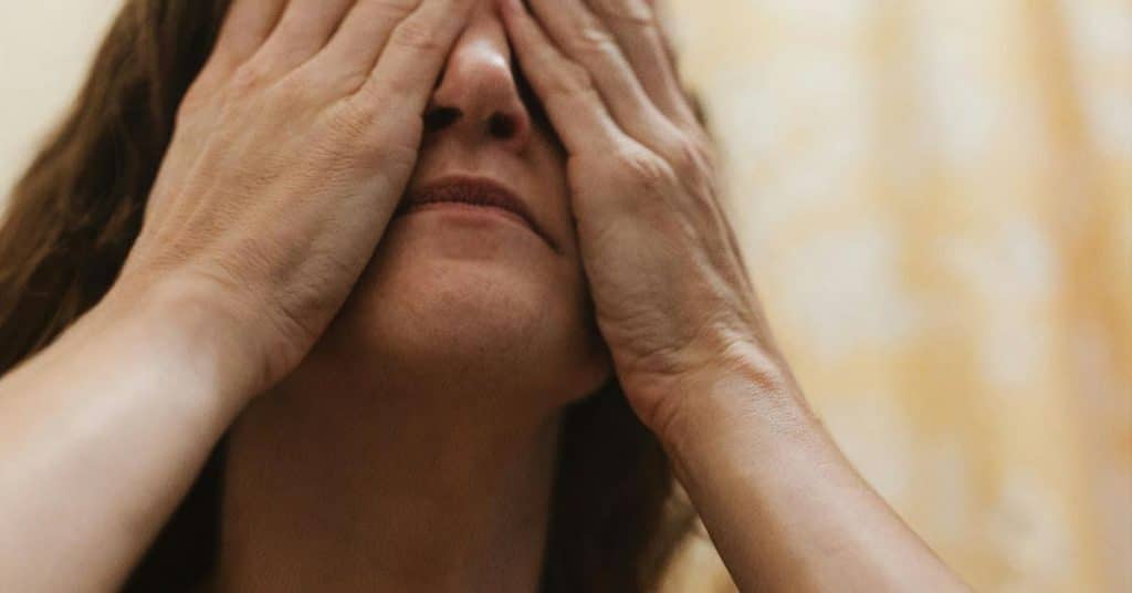 A person covering their eyes with both hands in soft light.