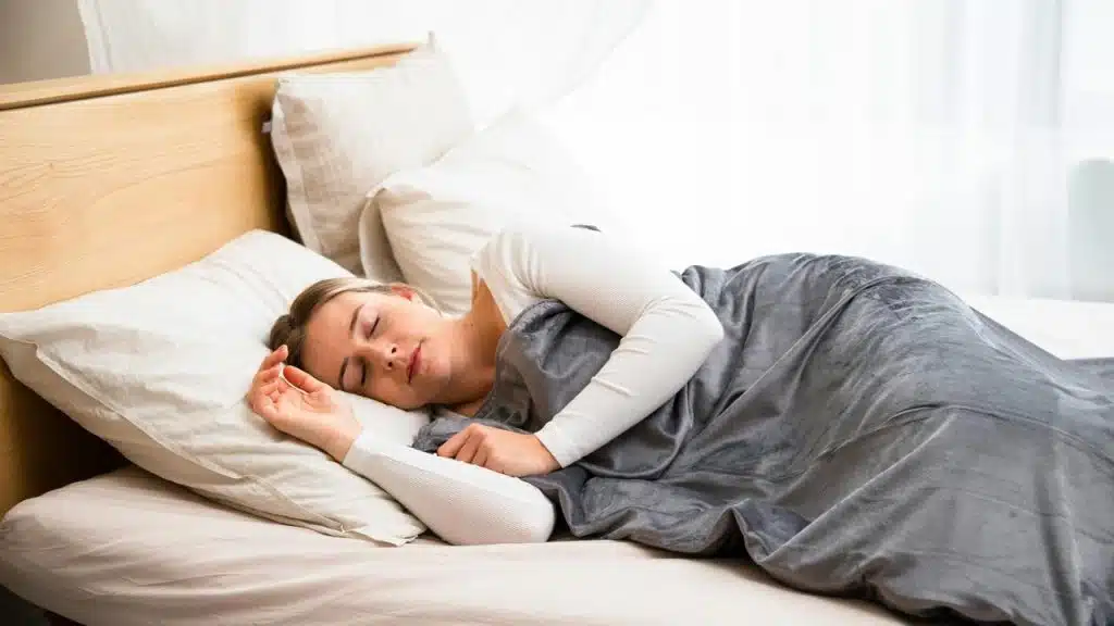A woman sleeping peacefully in bed under a gray blanket.