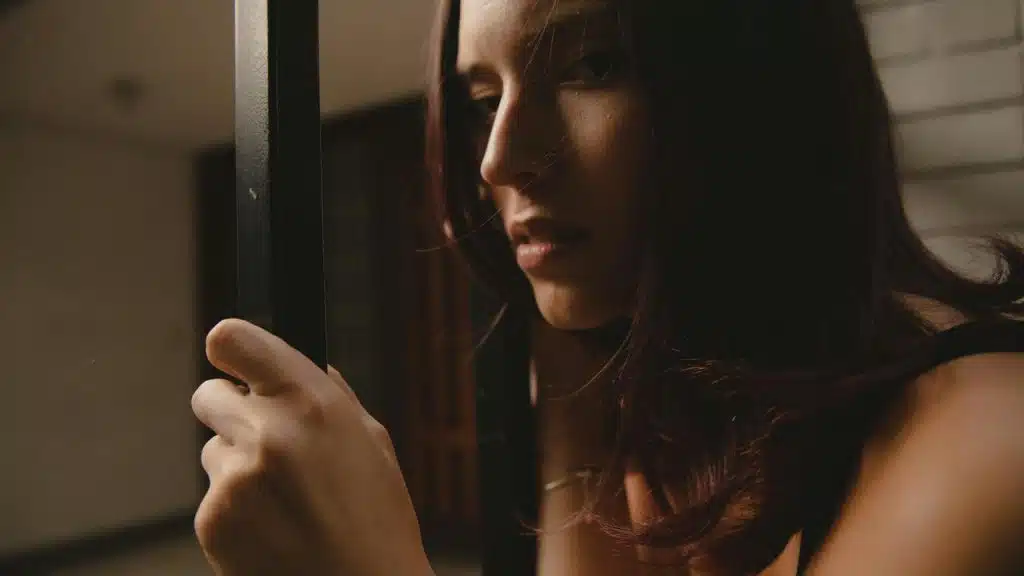A woman holding a doorframe and gazing thoughtfully in low light.