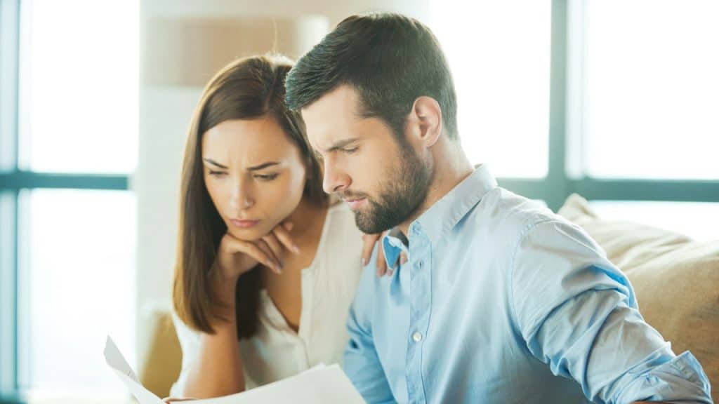 A man and woman sit together indoors while focusing their attention on a white paper.