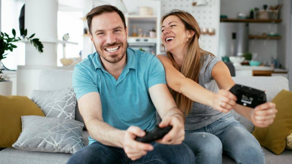 A smiling couple sitting on a couch playing video games together.
