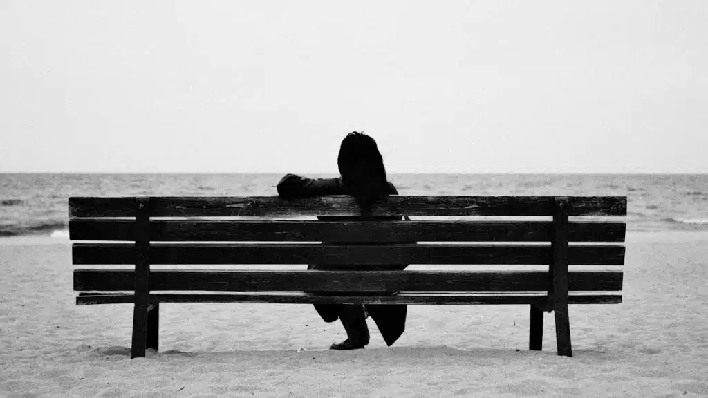 A person sits alone on a beach bench.