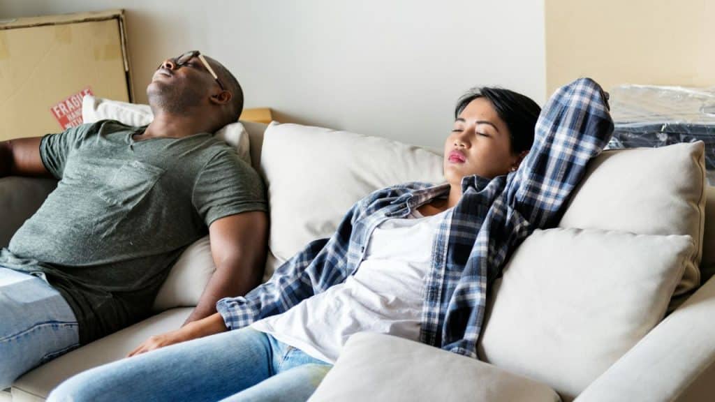 Two people lie back on a couch with their eyes closed in a bright room.