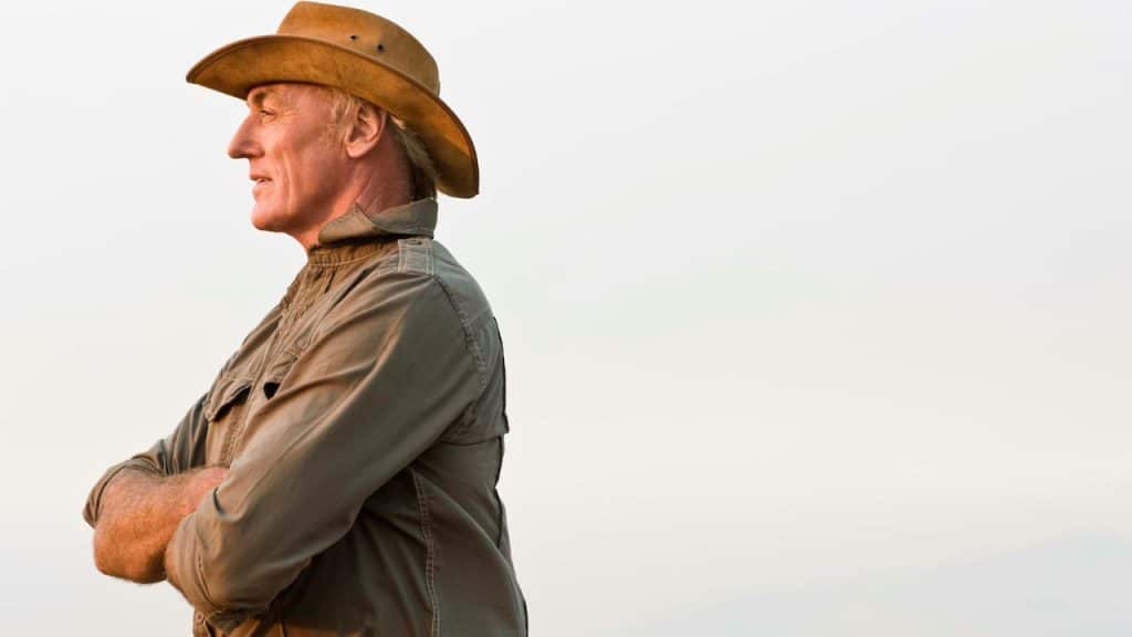 A man wearing a wide-brimmed hat standing outdoors with his arms crossed over his chest.