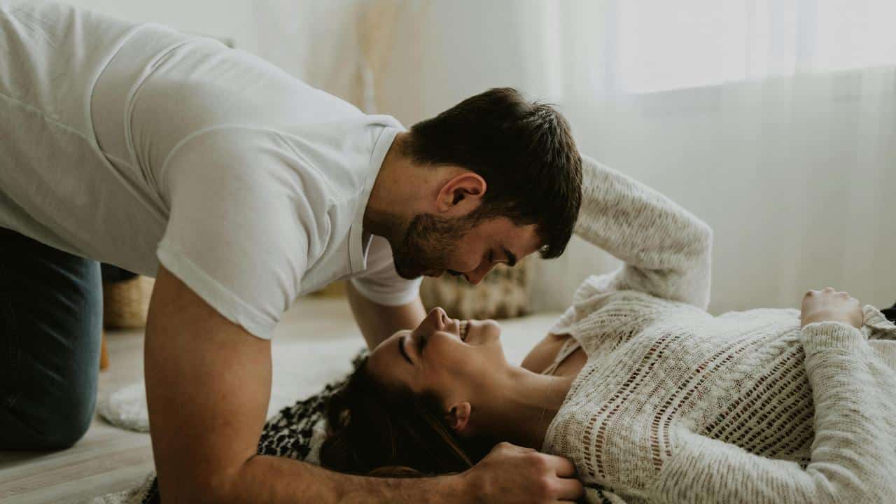 A couple smiling and gazing at each other while lying on the floor.