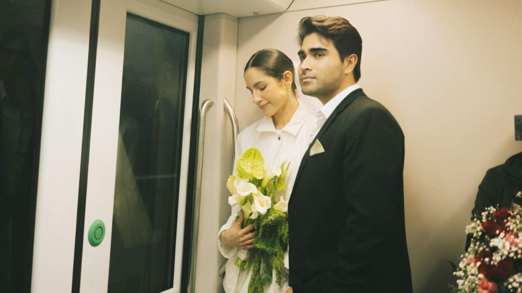 A man in a suit and a woman in white holding flowers on a train.