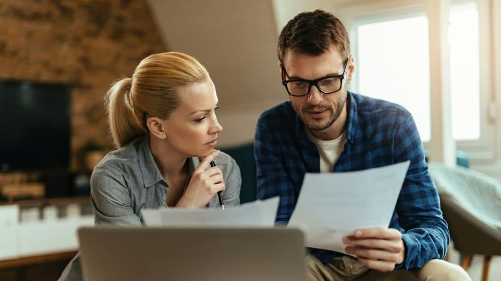 A woman with her hand on her chin looks at papers held by a man.