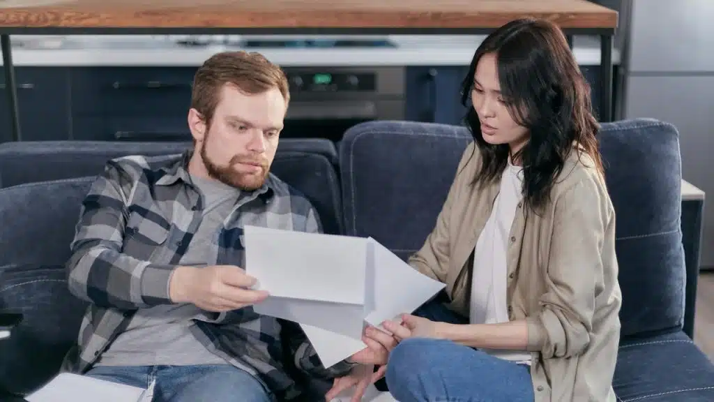 A man and woman sit on a dark blue sofa, looking together at several papers.