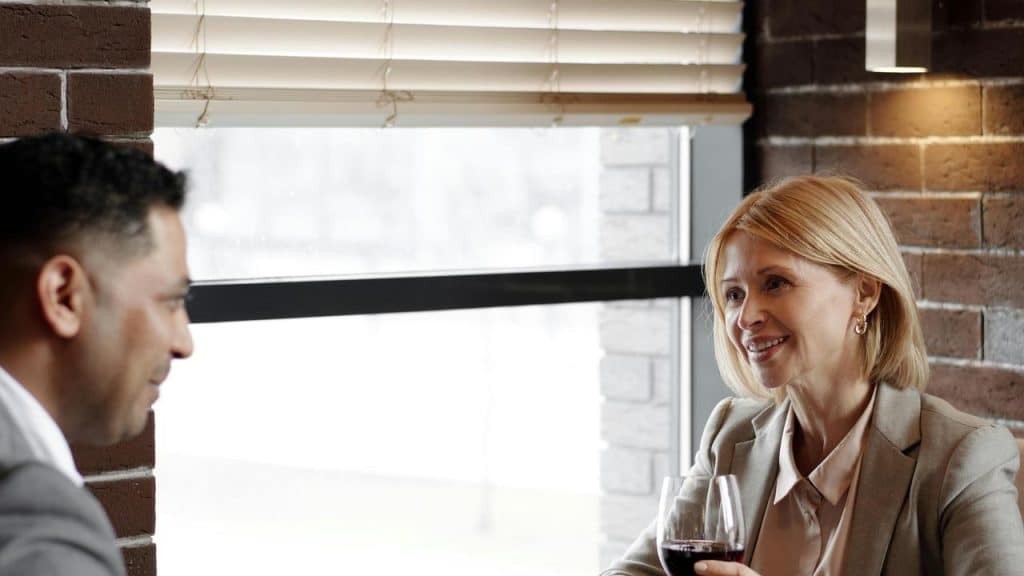 A man and woman sitting at a restaurant table smiling and talking over wine.