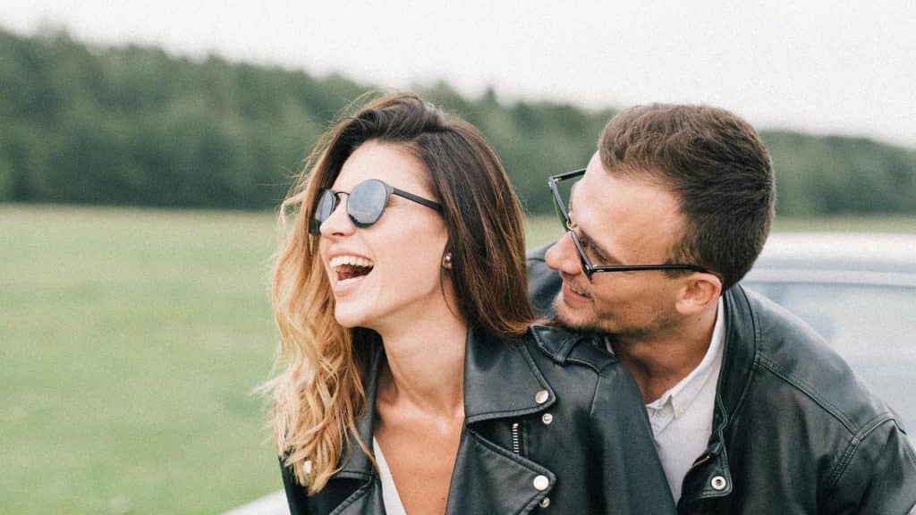 A couple wearing leather jackets laughing together outdoors.