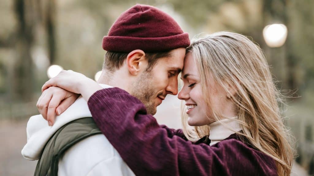 A man in a maroon beanie and a woman press their foreheads together while smiling.
