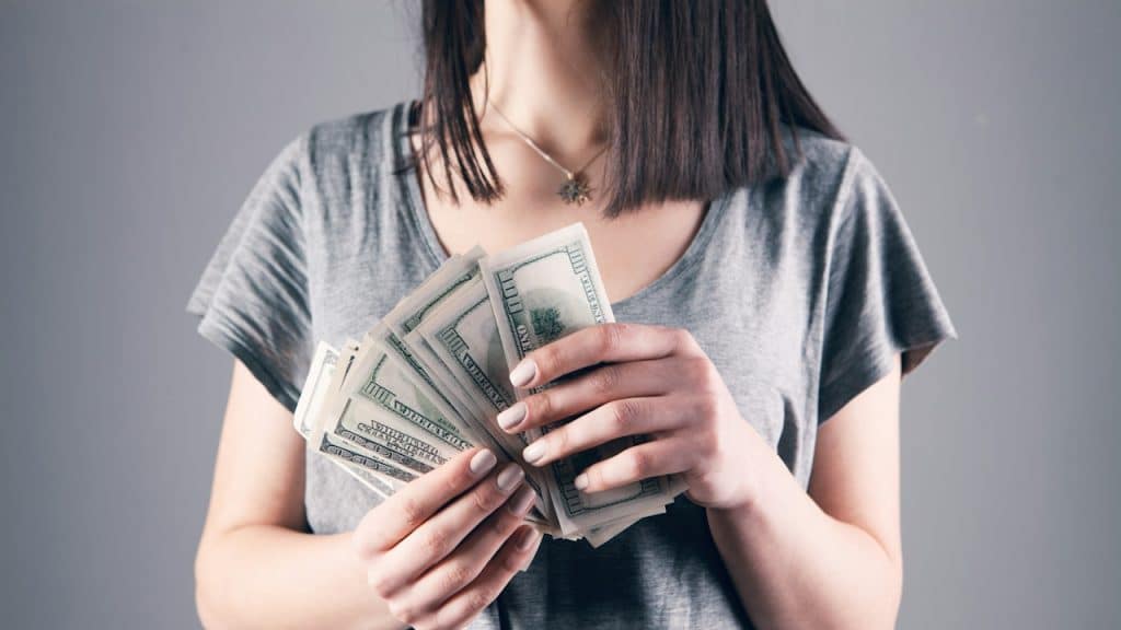 A woman holding several hundred dollar bills.