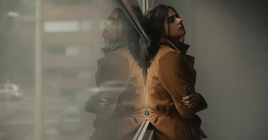 A woman leaning against a window with her reflection, appearing thoughtful.
