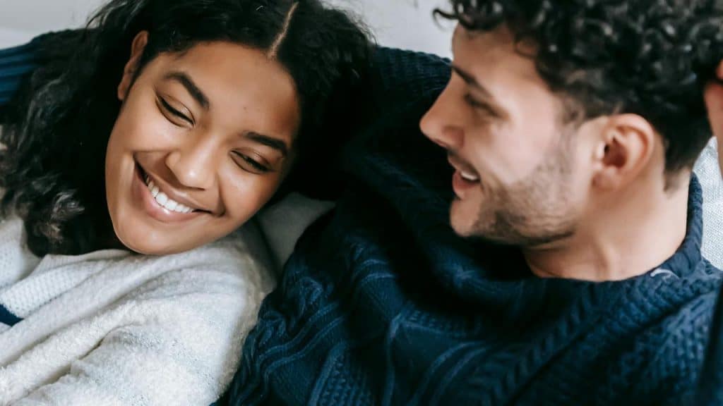 A couple lying together and smiling at each other on a couch.