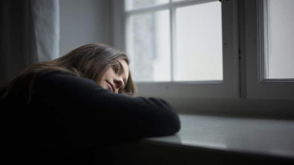 A woman resting her head on a table while looking out a window.